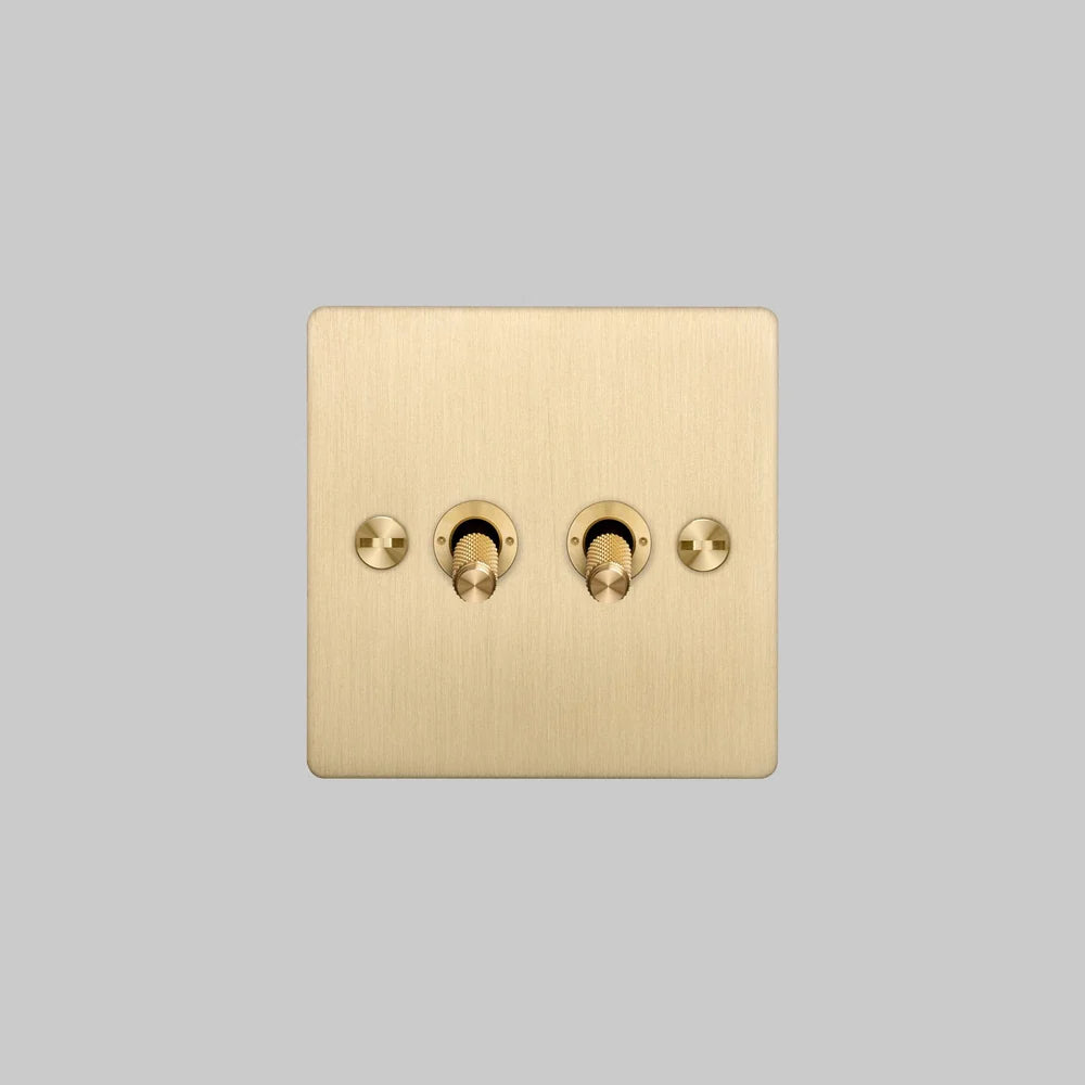 Buster + Punch 2G Toggle Light Switch in brushed brass, seen straight on with two knurled toggles and slotted screws