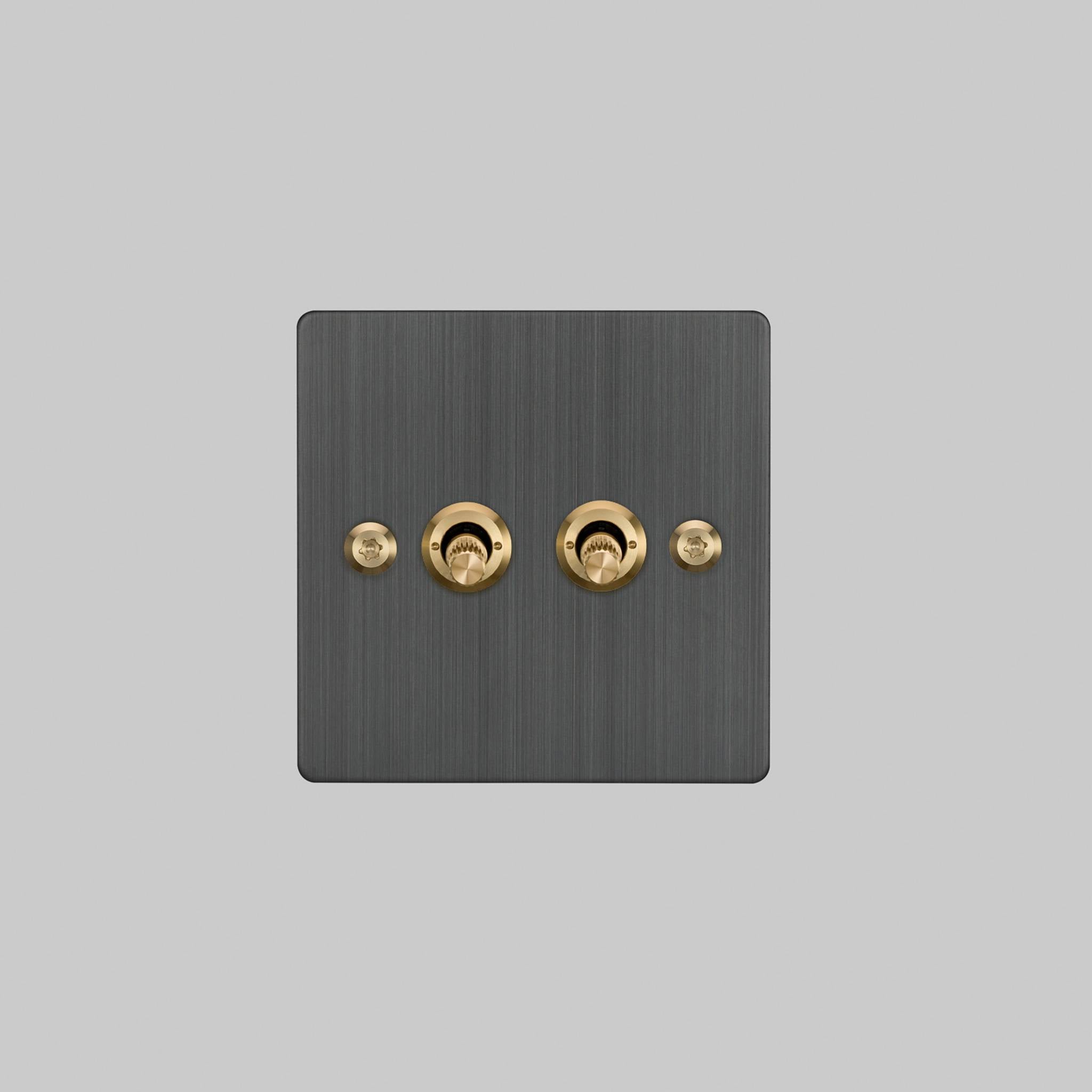 Buster + Punch 2G 2-way toggle switch, smoked bronze plate with brass linear knurl toggle arm, elevated angle view