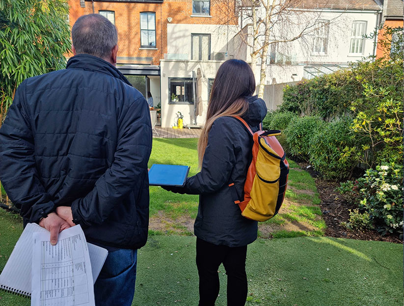 Two people standing in a garden with a house in the background