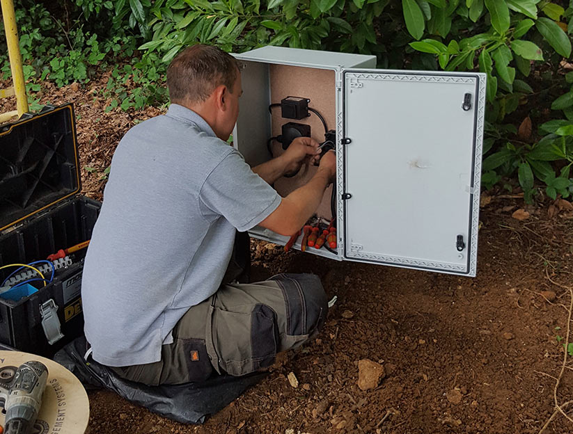 Person working on an outdoor electrical panel with tools and equipment nearby.
