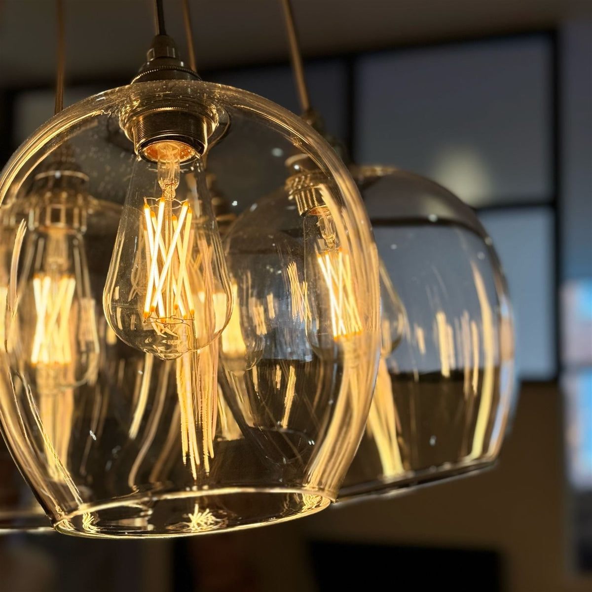 Close up of a clear glass pendant with a lit filament bulb and a brass toned lamp holder, with a second glass shade behind it