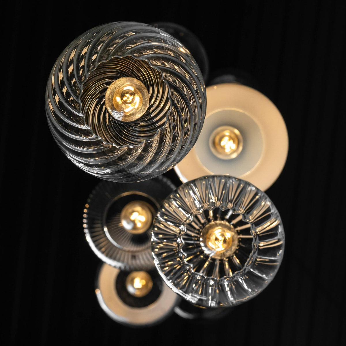 Group of lit pendants with swirled, ribbed and opal glass shades photographed against a black background