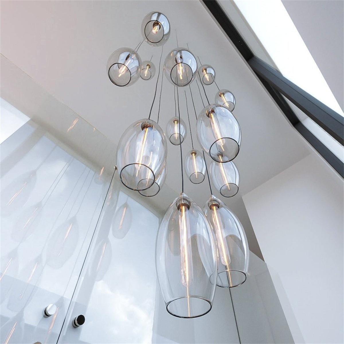 Leverint Bespoke Cascade Pendant Cluster, clear glass pendants in several shapes and sizes hanging at different heights in a double height space, photographed looking upwards