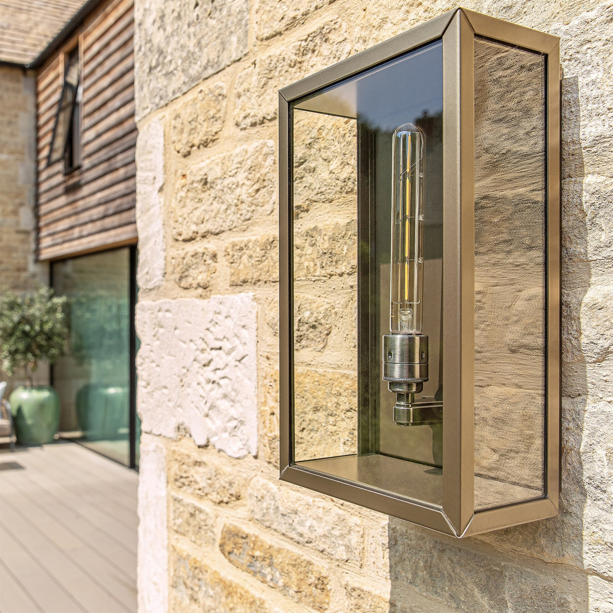 Leverint Chelsea wall lantern with glass panels and a tube filament bulb, fitted to a sunlit stone wall outdoors