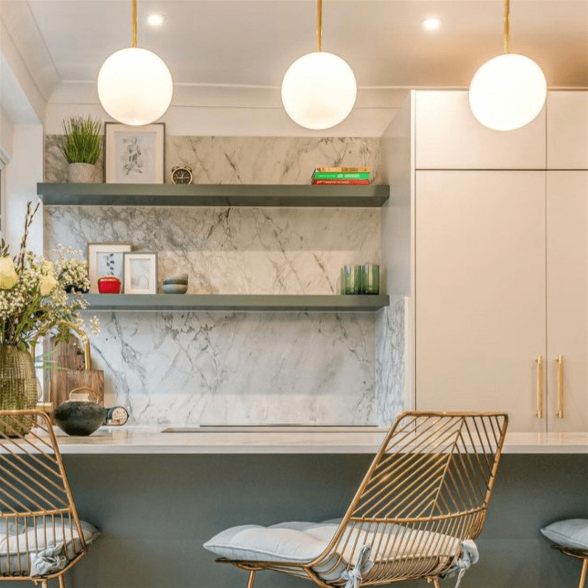 Leverint Pimlico sealed rod pendants with three opaque white glass spheres on brass rods above a breakfast counter in a marble kitchen (lifestyle photo, size may differ from the Mini)