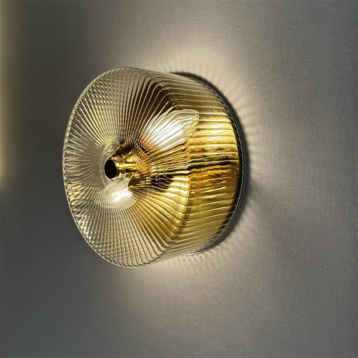 Leverint Temple Flush Mount in fine ribbed glass with a brass finish inside, lit against a grey wall, fine ribs radiating from the centre