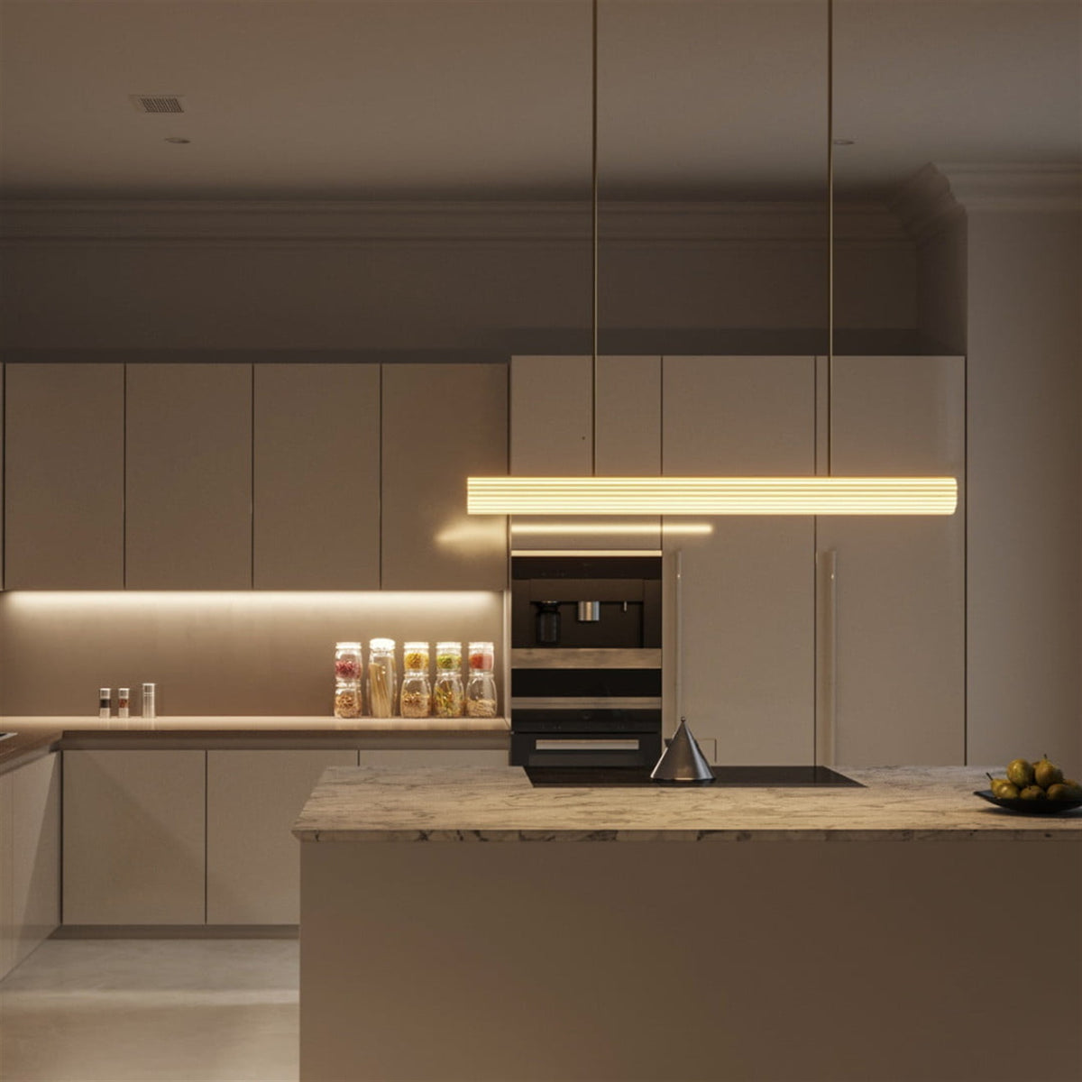 Leverint Temple Rod Pendant, a long ribbed glass bar on two slim brass rods, lit warm white in a contemporary kitchen (lifestyle photo, length may differ from the Medium)