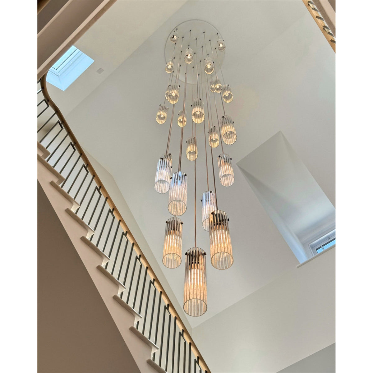 Leverint Temple Pendant Cluster, many fluted clear glass cylinder pendants hanging at different heights from a round white ceiling plate, seen from below in a stairwell