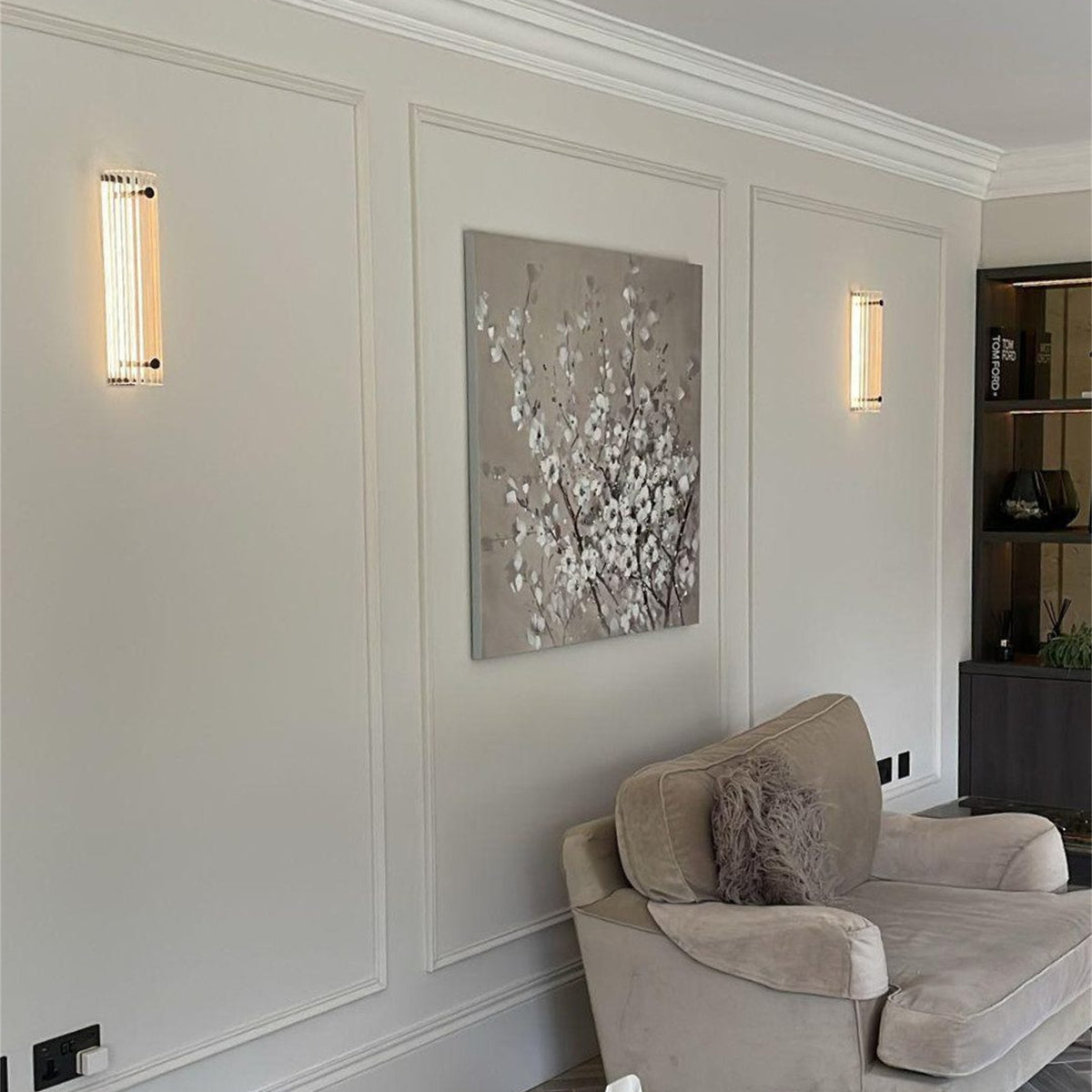 Two lit Leverint Temple Pillar Lights on a panelled living room wall either side of a framed picture, with an armchair below