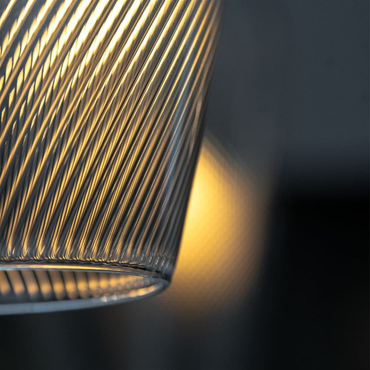 Close up of the lower rim of a spiral ribbed clear glass shade lit warm amber against a dark background