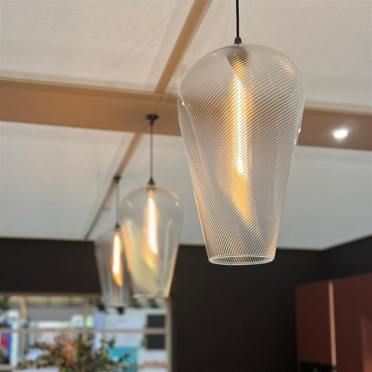 Spiral ribbed clear glass pendants lit with filament bulbs indoors, one in sharp focus with another blurred in the foreground